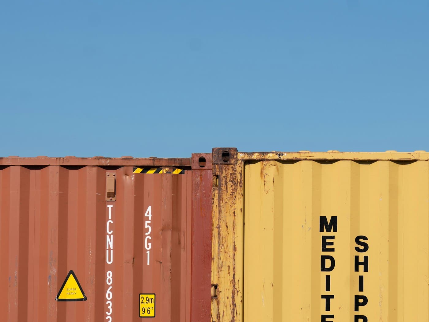 Stacked shipping containers in orange and teal against a clear blue sky