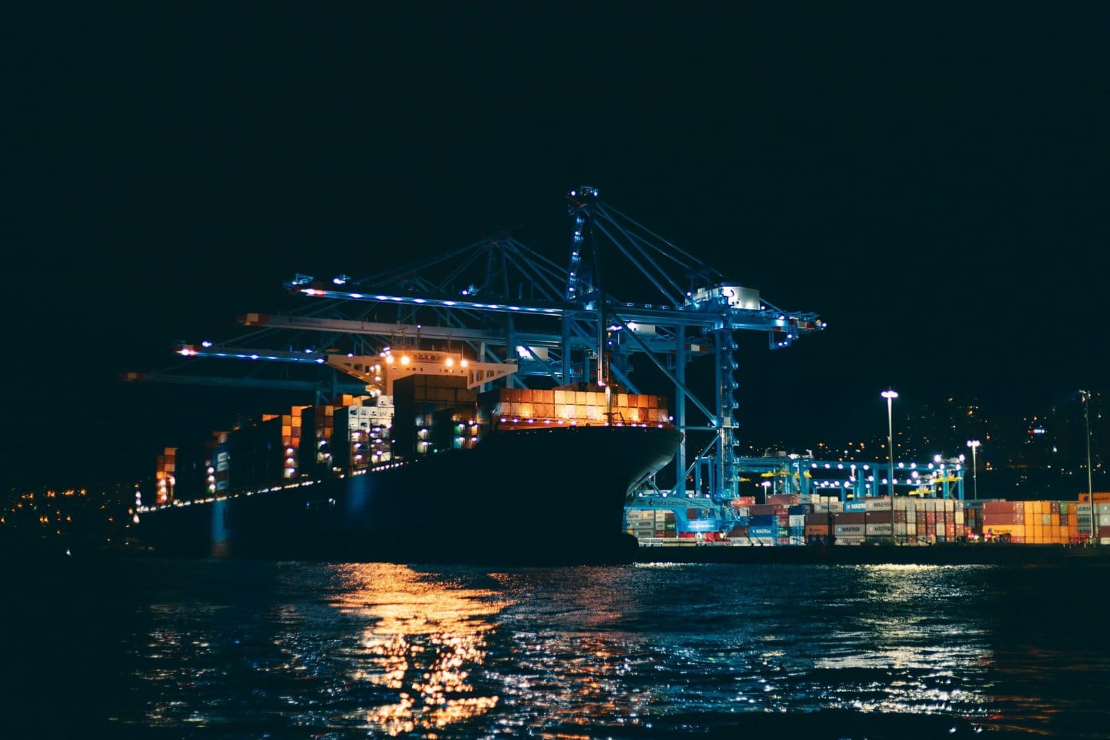A cargo ship berthed at a brightly lit port at night