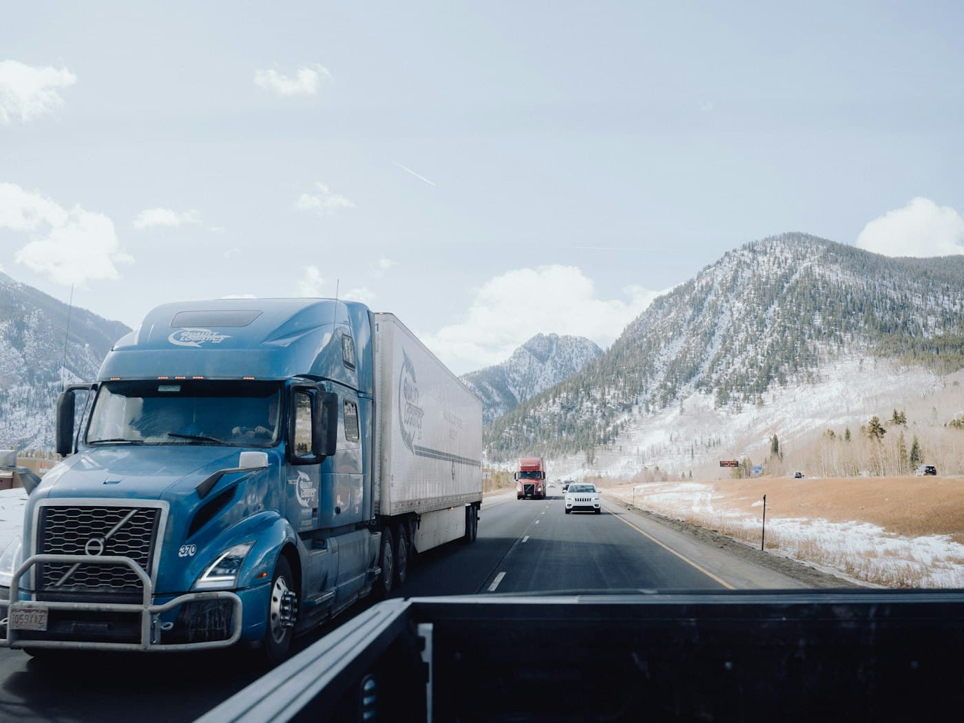 A freight truck on a winding mountain road between snow-covered peaks